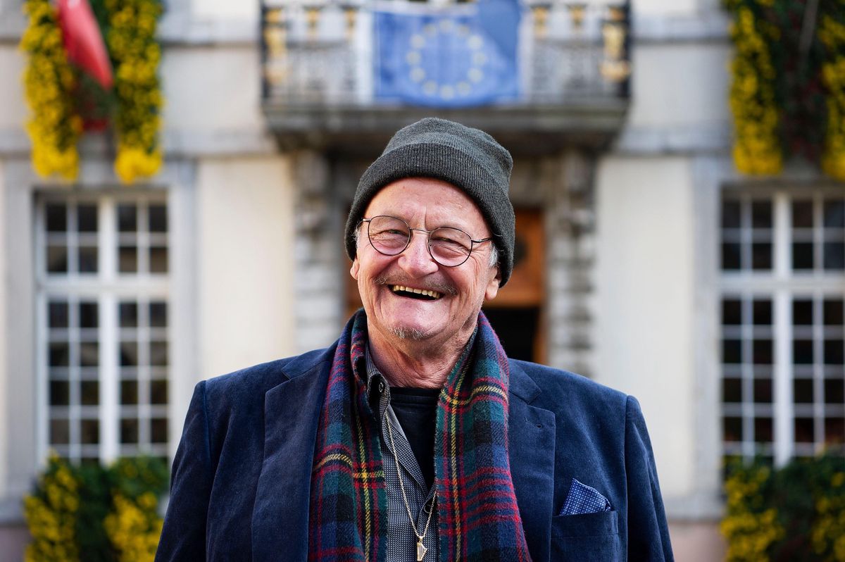 Un homme souriant portant un bonnet et une écharpe sourit devant un bâtiment décoré de fleurs jaunes à Vevey, le 26 octobre 2018.
