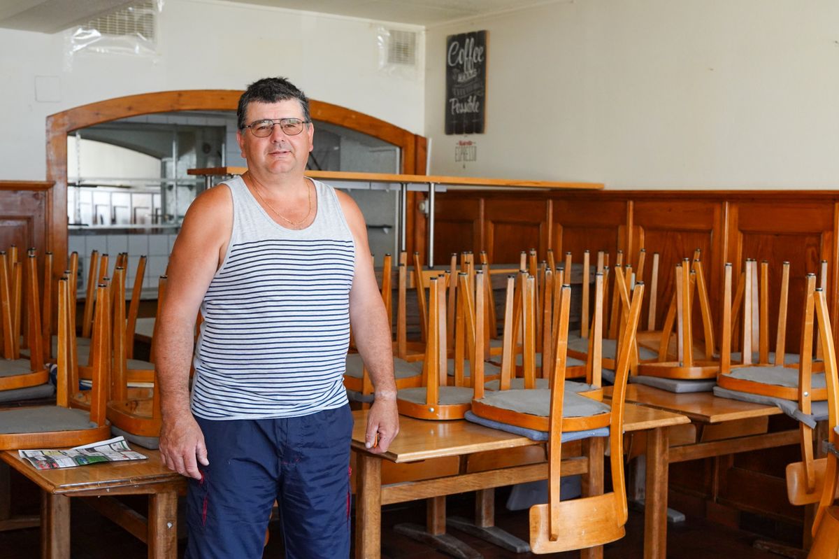 Un homme en débardeur rayé se tient debout dans un restaurant avec les chaises empilées sur les tables.