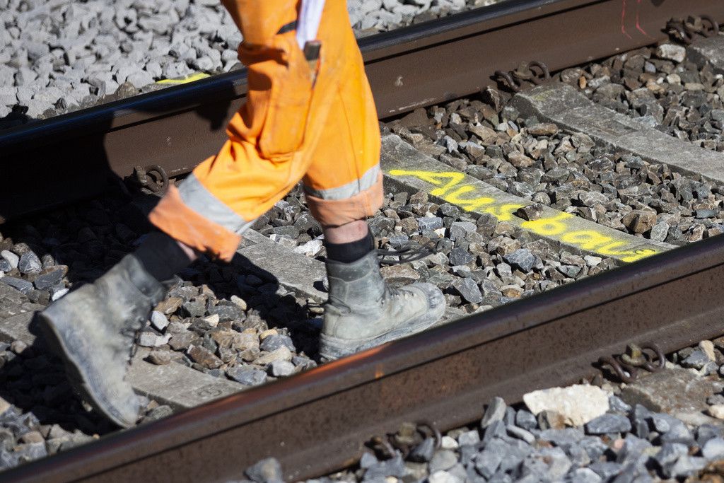 Un travailleur en tenue orange marche sur une voie ferrée avec une marque 'Ausbau' pendant les travaux sur la ligne entre Fribourg et Berne.