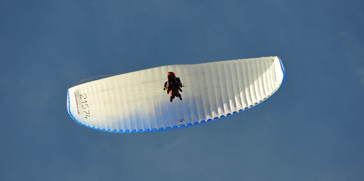 Ein Gleitschirmflieger schwebt am blauen Himmel.