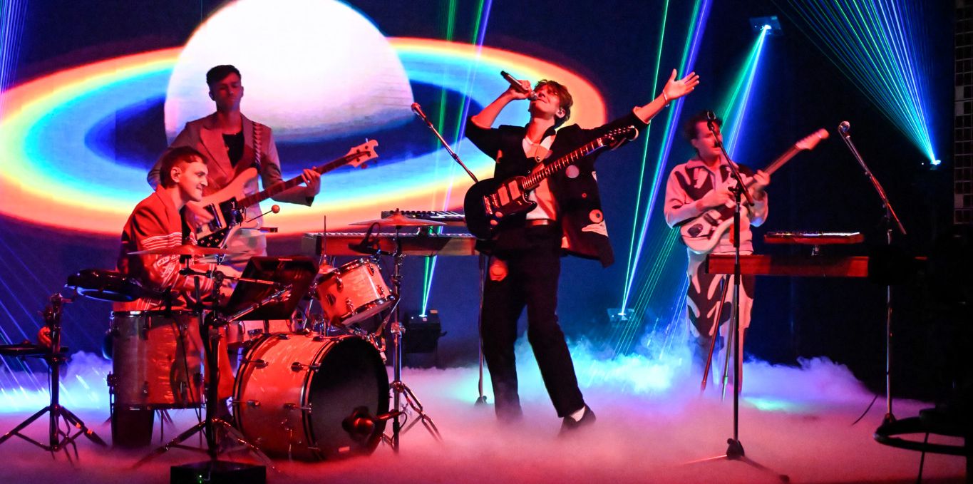 Le groupe Glass Animals se produit sur scène à l'émission 'The Tonight Show', avec des instruments et des effets lumineux colorés dans le fond.