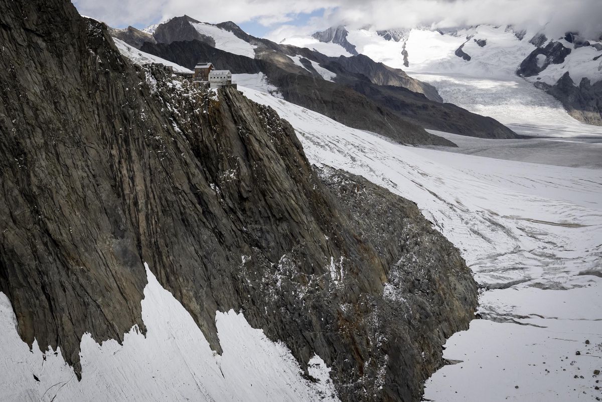 Vue aérienne de la cabane Hollandiahuette au sommet d’une falaise enneigée avec des glaciers en arrière-plan dans la vallée du Lötschental, Valais.