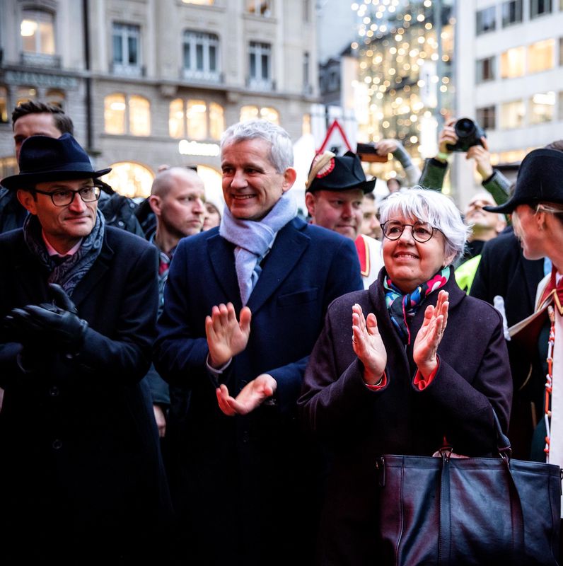 Menschenmenge applaudiert bei der Bundesratsfeier von Beat Jans in der Innenstadt, im Hintergrund weihnachtliche Beleuchtung.