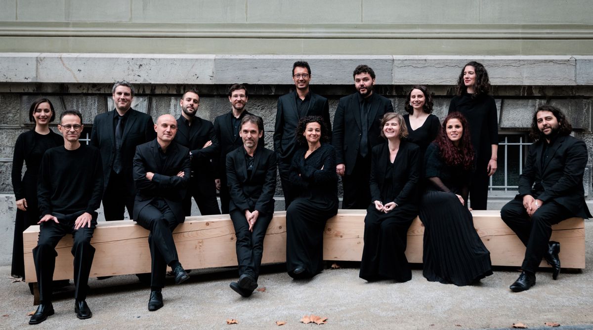 Un groupe de quinze personnes posant ensemble, tous vêtus de noir, devant un bâtiment en pierre.