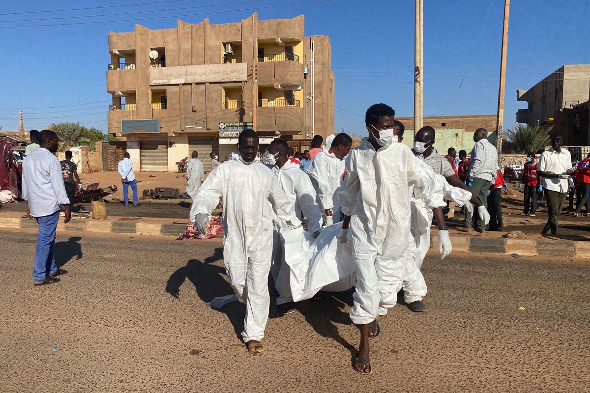 Des secouristes en combinaisons blanches transportent une civière dans une rue bordée de bâtiments.