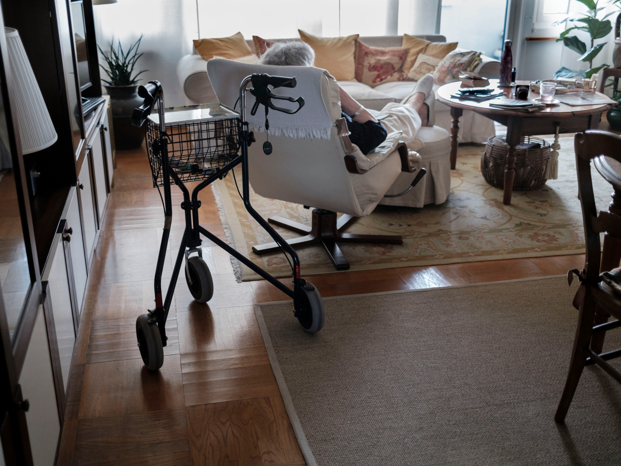 Une femme âgée se repose dans un fauteuil dans un salon confortable à Genève, avec un déambulateur à proximité.