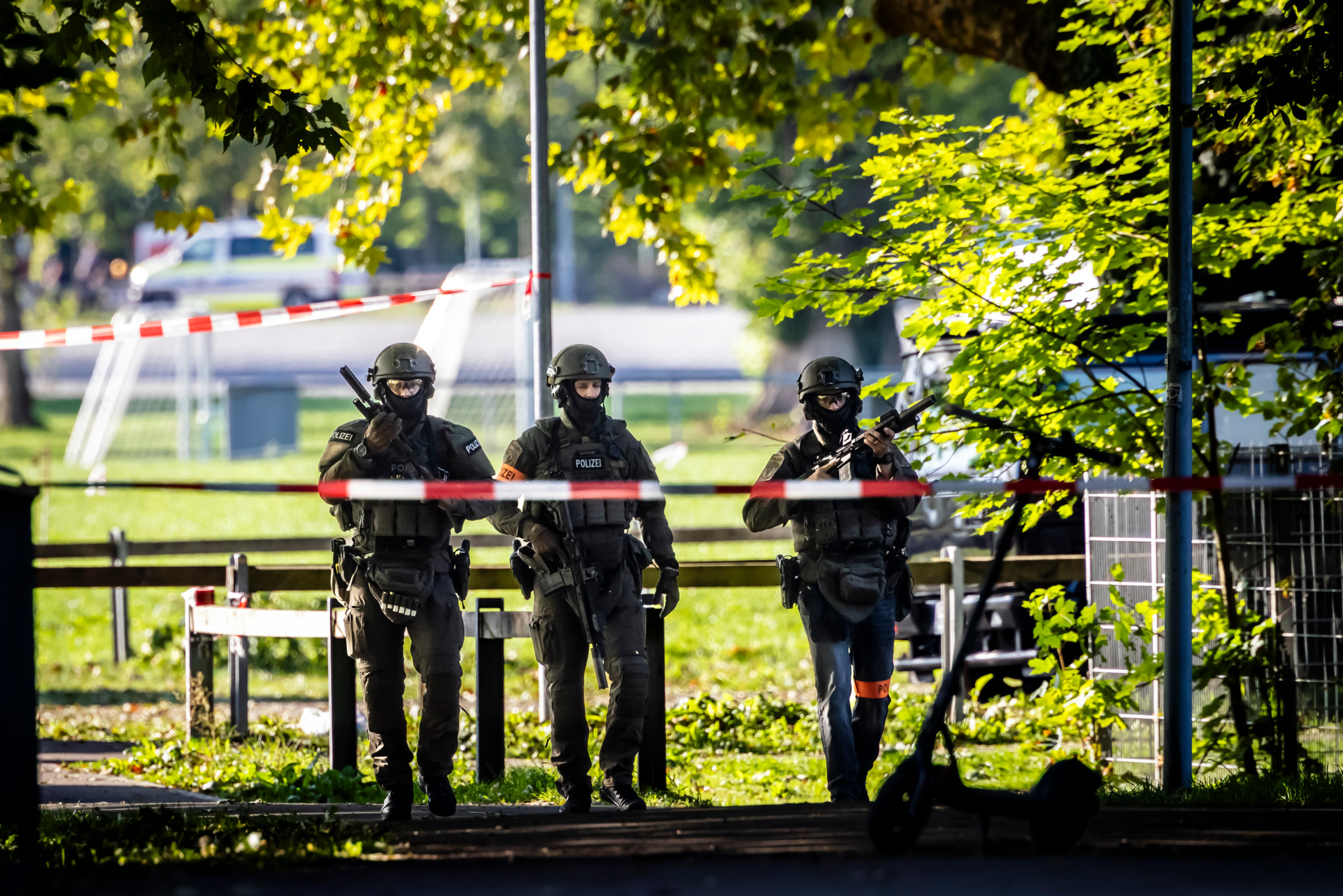 Drei bewaffnete Polizisten in Schutzausrüstung patrouillieren hinter Absperrband beim Pferderennplatz Schachen in Aarau nach einer Schiesserei.
