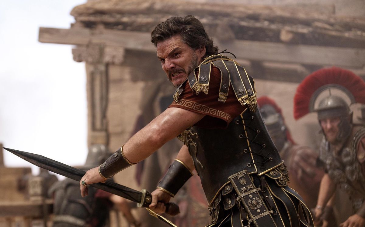 Ein Krieger in antiker Rüstung mit Schwert im Kampf, umgeben von anderen Soldaten vor einer hölzernen Struktur.