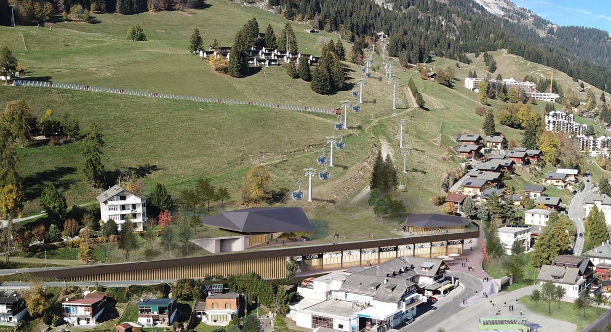 Vue aérienne d'un village alpin avec de nombreuses maisons, des collines verdoyantes et des montagnes en arrière-plan.