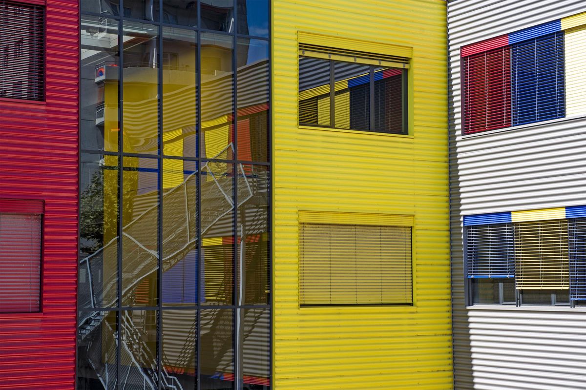 Façade colorée de l’Ecole cantonale d’art de Lausanne à Renens, avec des panneaux rouges, jaunes et gris et des fenêtres avec stores.