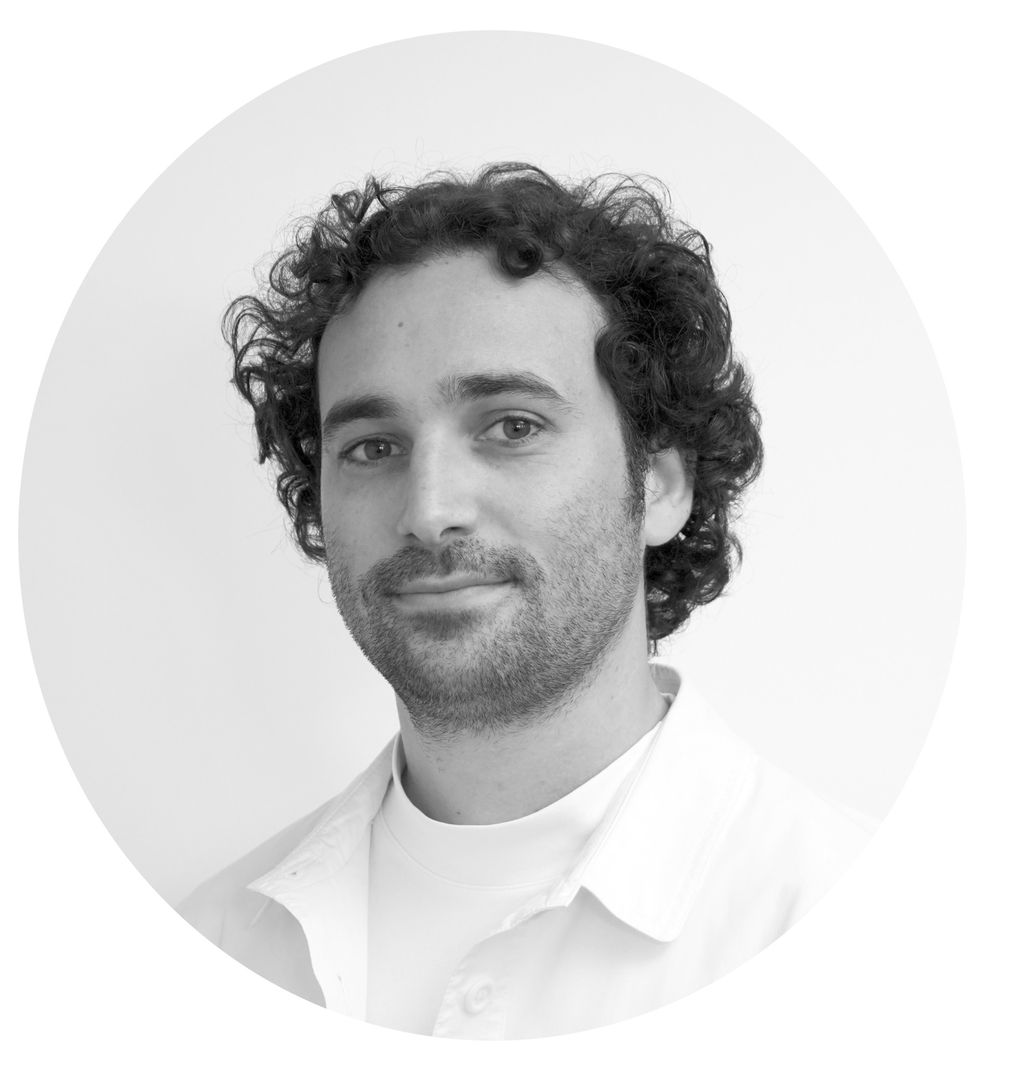 Portrait en noir et blanc d'un homme avec des cheveux bouclés et une barbe légère, portant une chemise claire.