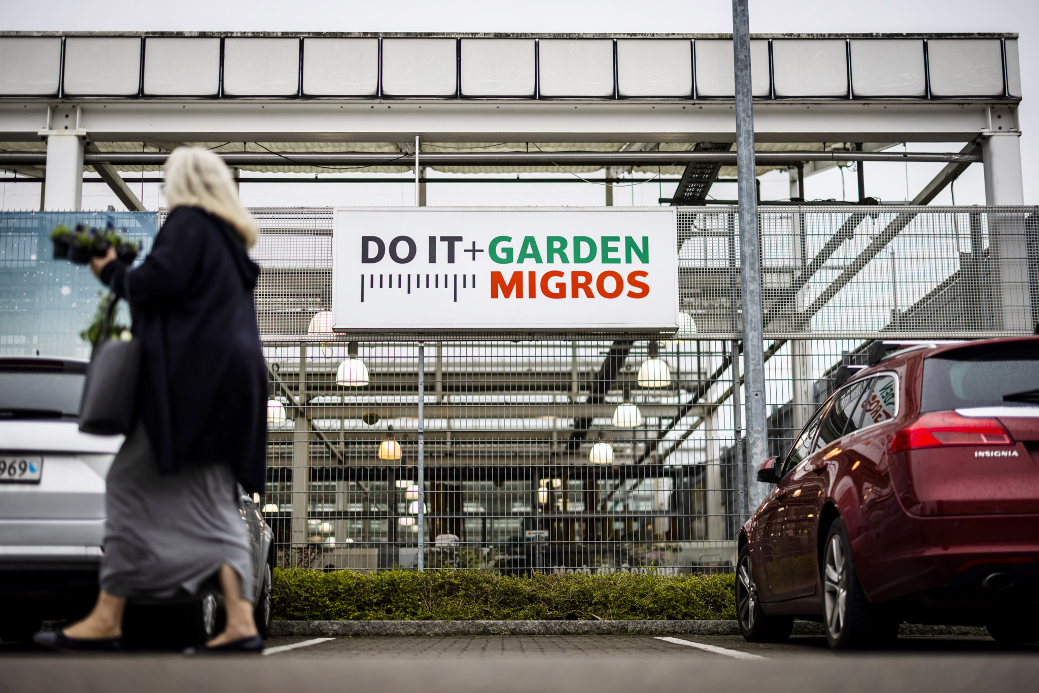 Eine Frau geht an einem Schild der Do it + Garden Filiale von Migros in Bülach vorbei. Im Hintergrund ist der Eingang zum Geschäft zu sehen.