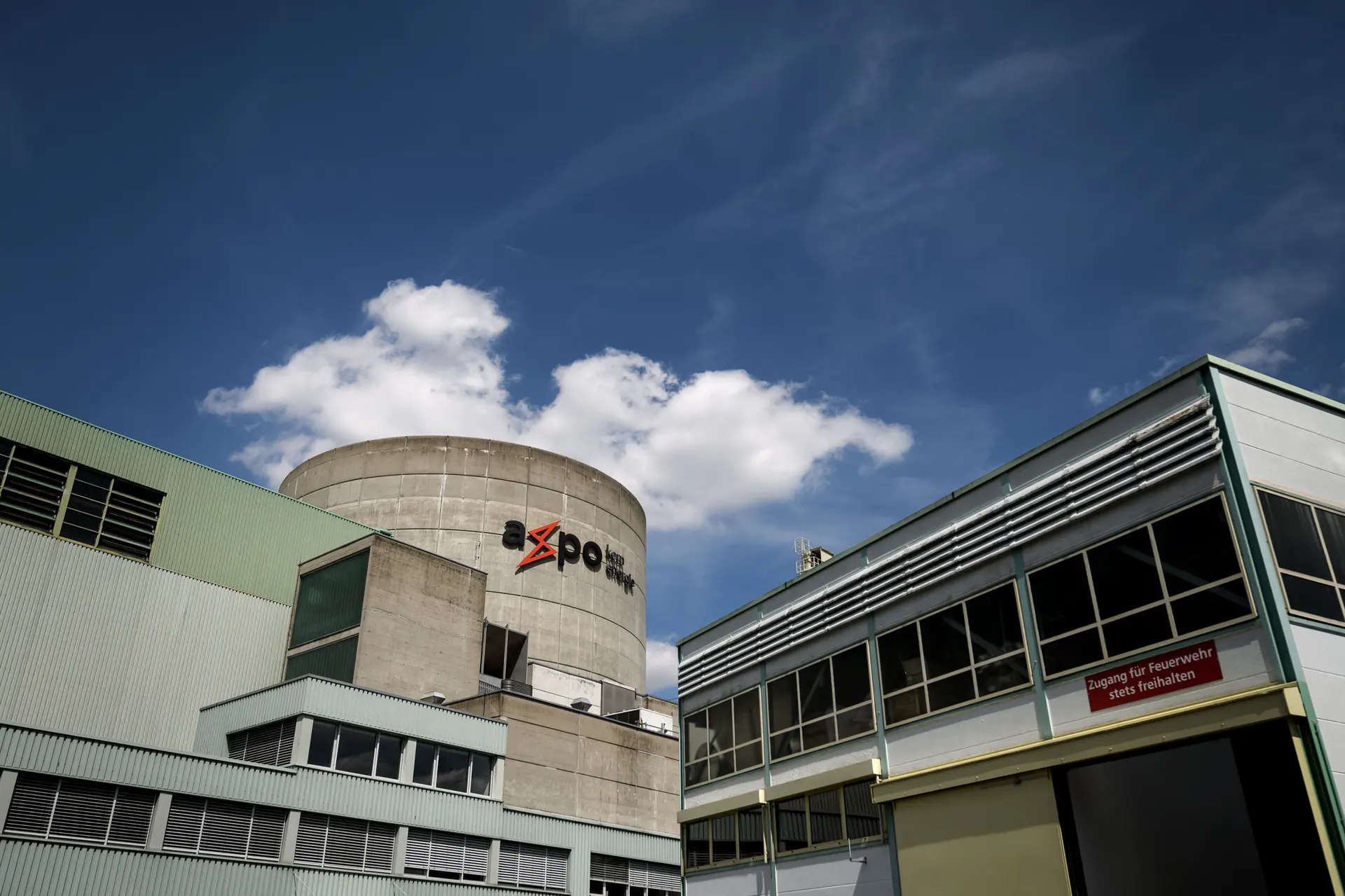 Centrale nucléaire avec logo Axpo sur la tour, ciel bleu et quelques nuages en arrière-plan.