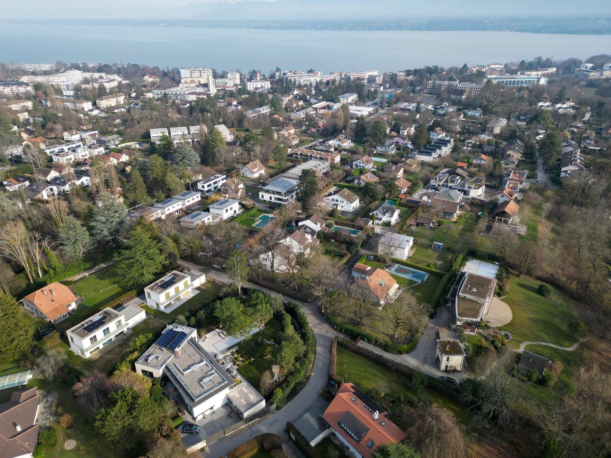 Vue aérienne d’une zone résidentielle pavillonnaire à Versoix, avec de nombreuses maisons entourées de végétation et un aperçu du lac au fond.
