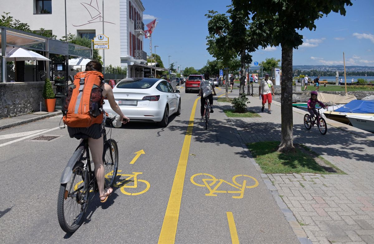 Des cyclistes et des piétons partagent une voie en bord de lac à Morges, où une voiture empiète sur la zone piétonne au quai du Mont-Blanc, un dimanche.