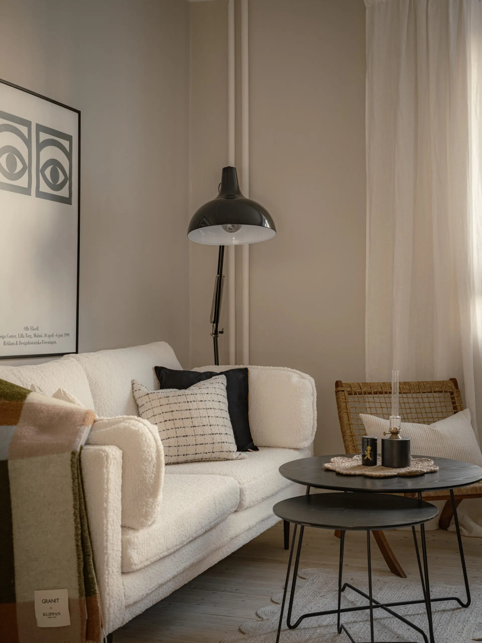 Elegantes Wohnzimmer mit weissem Sofa, schwarzer Stehlampe, runden Beistelltischen und einem Rattanstuhl in warmen Erdtönen.