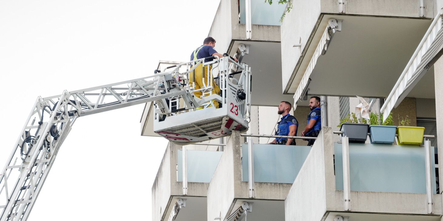 Des pompiers sur une nacelle atteignent les balcons d'un immeuble résidentiel, parlant avec des résidents.