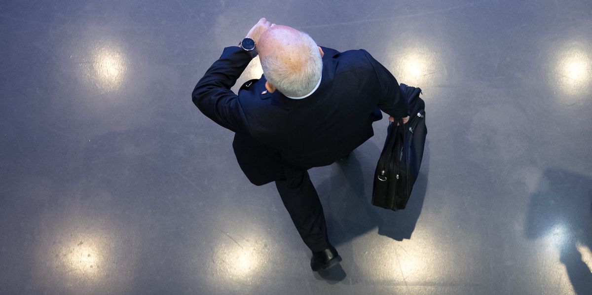 Homme vêtu d'un costume sombre portant une mallette, vu de dessus, marchant sur un sol gris avec des lumières reflétées.