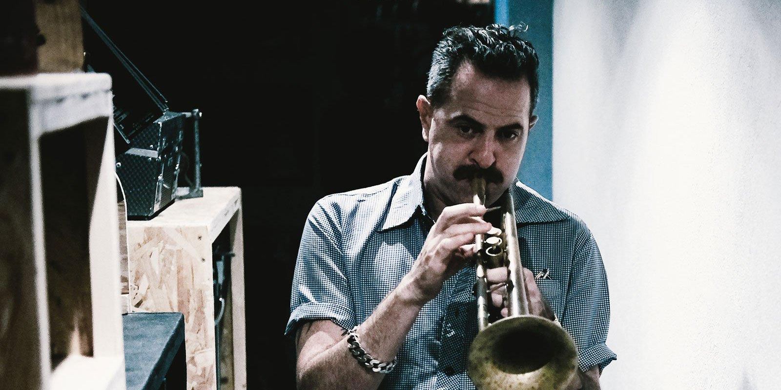 Un homme joue de la trompette dans un couloir étroit, entouré de caisses en bois.