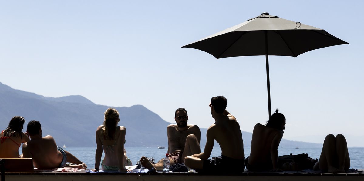 People take a break under an umbrella and enjoy the warm summer weather on the shores of Lake Geneva in front of the Swiss Alps mountains, in Vevey, Switzerland, Saturday, July 8, 2023 (KEYSTONE/Cyril Zingaro)