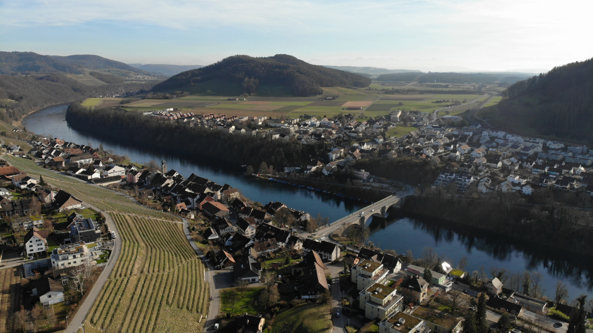 Luftaufnahme von Eglisau mit Blick auf die Rheinbrücke im Zentrum, umgeben von Landschaft und Gebäuden.
