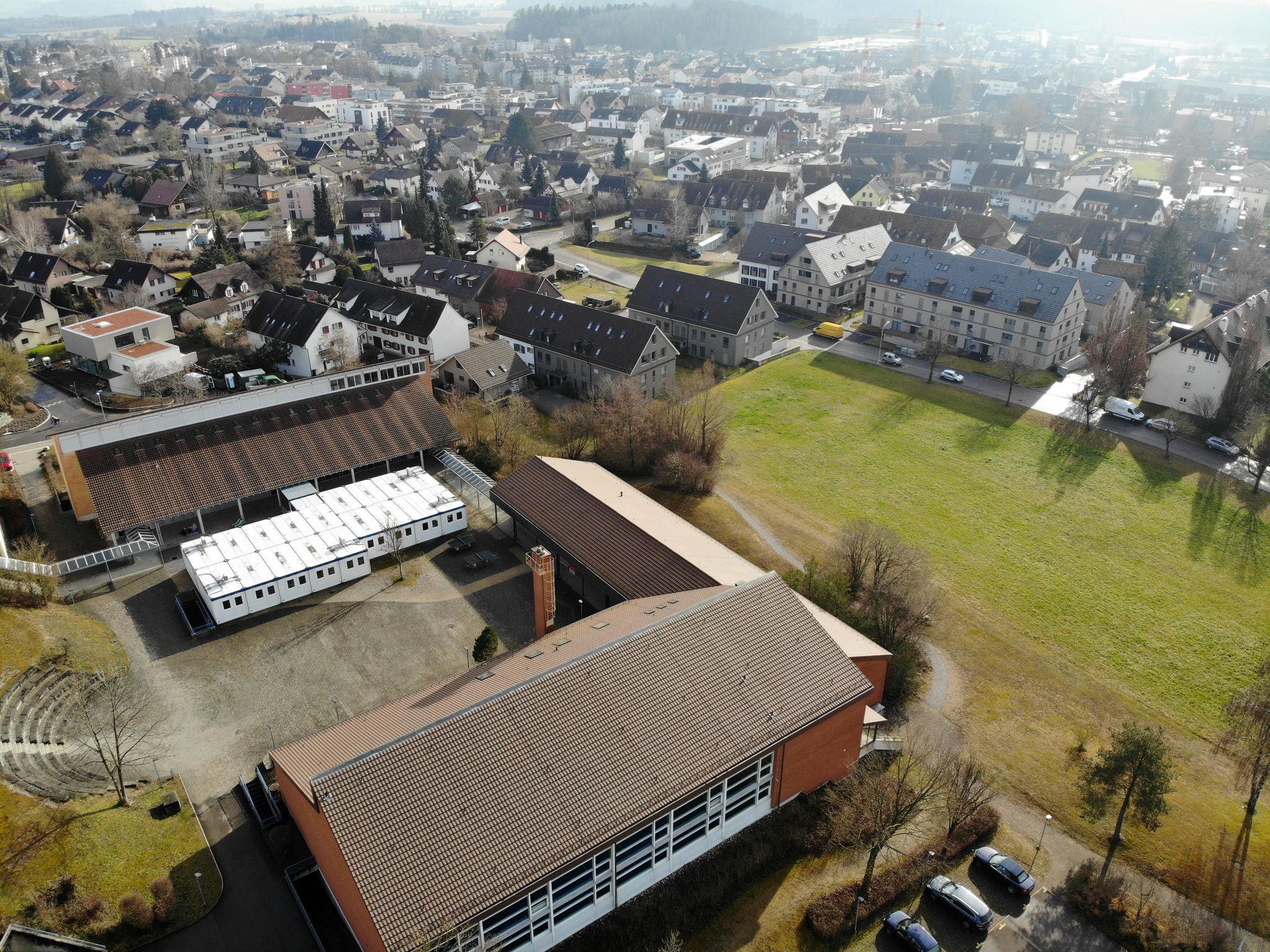 Das Gelände der Sekundarschule Seuzach vom Westen her betrachtet: Weiss sind die provisorischen Container sichtbar, in denen sich das momentane Pilotprojekt befindet. Das geplante Bauprojekt sähe einen Umbau das Trakts 1 (nicht im Bild) und eine Verbindung der Trakte 3 und 4 (Lücke rechts der Container) vor.