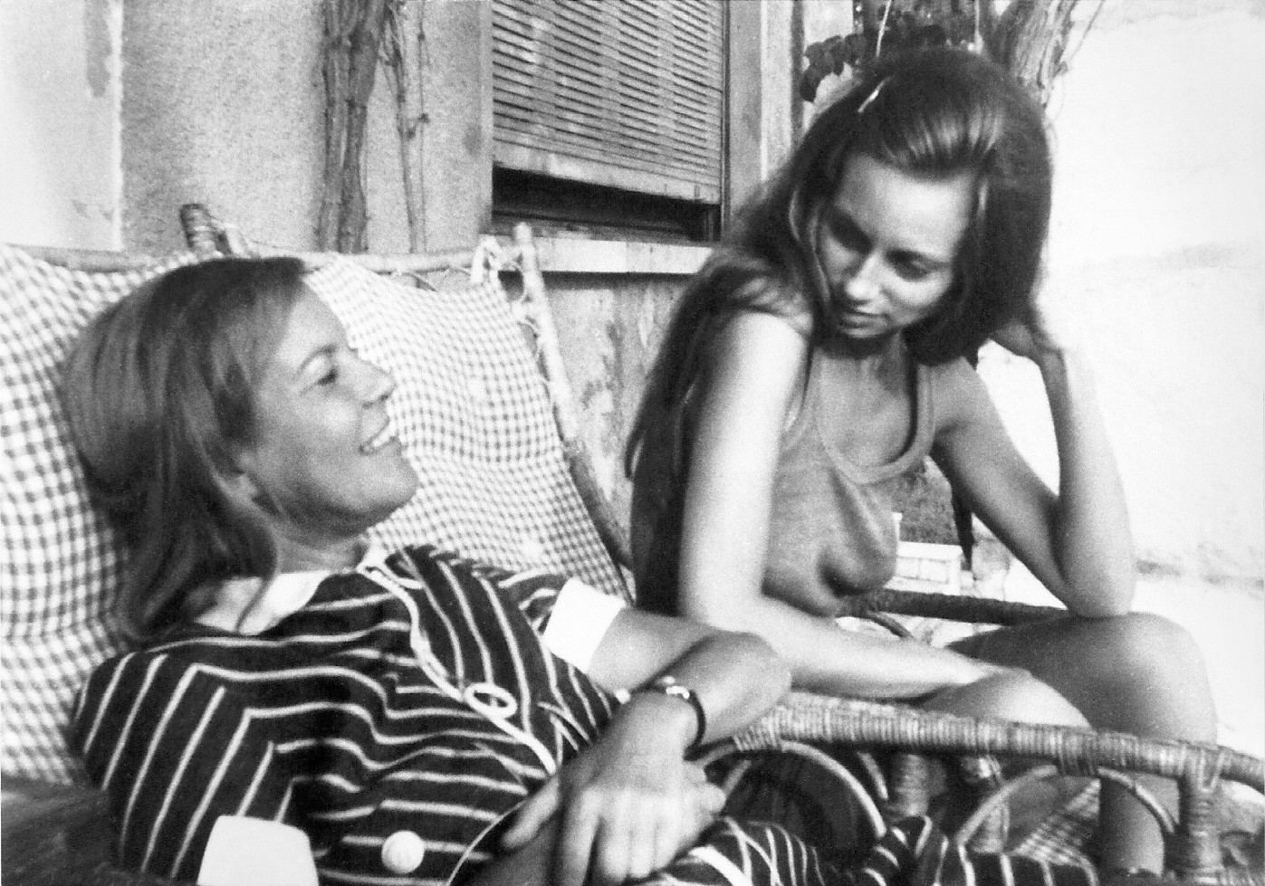 Zwei Frauen sitzen auf Korbstühlen und unterhalten sich, Schwarz-Weiss-Aufnahme im Vintage-Stil der 1970er-Jahre.