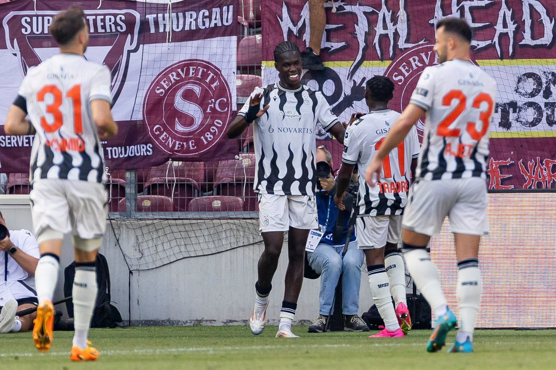Basel-Spieler Dominik Schmid, Torschütze Thierno Barry, Adama Traore und Albian Ajeti feiern ein Tor gegen Servette FC im Super League-Spiel in Genf. Banner und Tribüne im Hintergrund. Basel-Spieler Dominik Schmid, Torschütze Thierno Barry, Adama Traore und Albian Ajeti feiern ein Tor gegen Servette FC im Super League-Spiel in Genf. Banner und Tribüne im Hintergrund.