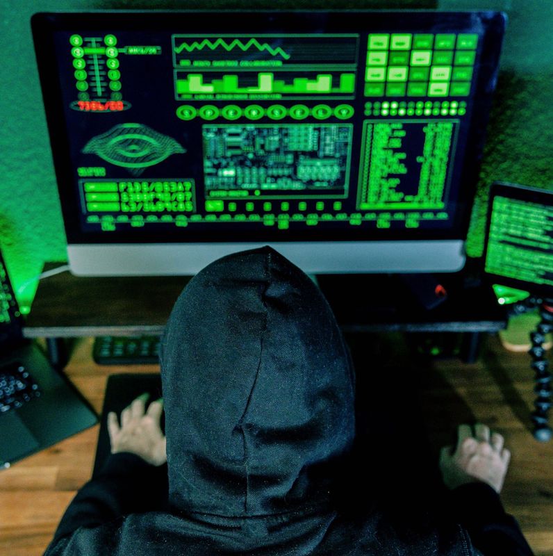 Person in Kapuzenpullover an einem Computer mit grüner Codeanzeige, Symbolbild für Hacker und Internetkriminalität.