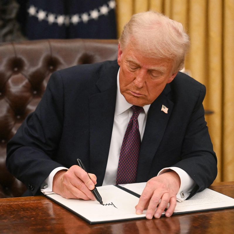 Un homme assis dans le Bureau ovale de la Maison Blanche signe un document officiel avec un stylo noir.