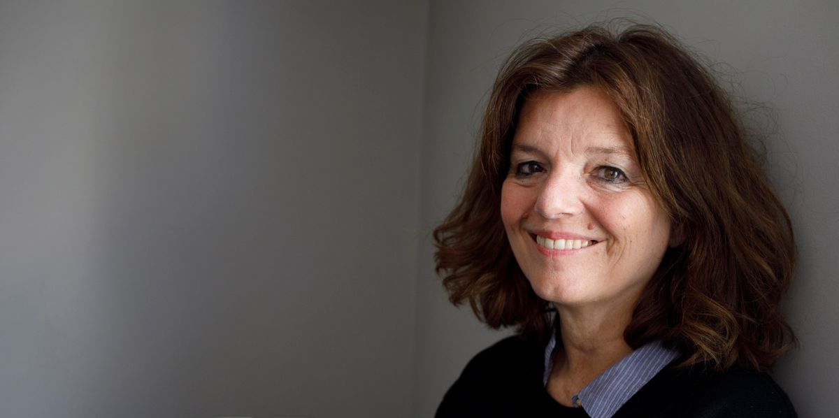 Portrait de Maylis de Kerangal, auteur, assise contre un mur gris, souriante, le 18 mars 2023. ©Basso Cannarsa/opale.photo