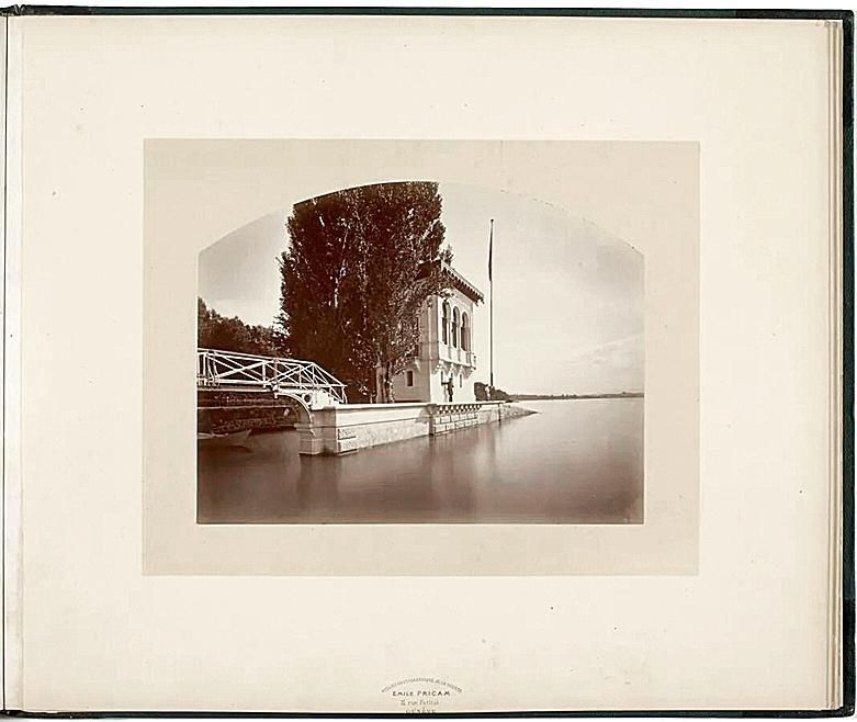 Maison au bord du lac avec un pont en bois et des arbres en arrière-plan.