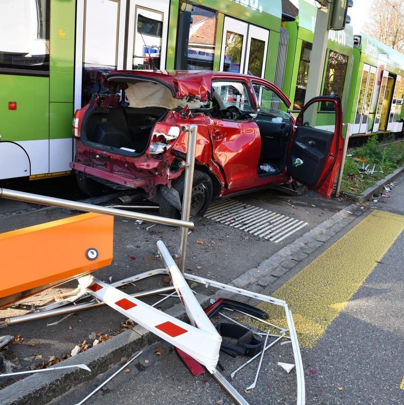 Ein rotes Auto mit schweren Heckschäden nach einem Zusammenstoss mit einem grünen Strassenbahnwagen. Beschädigte Verkehrsschilder liegen auf dem Boden.