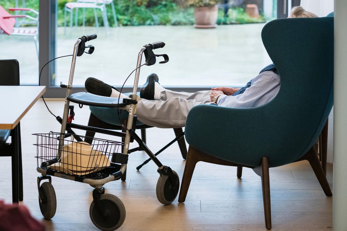 Un résident atteint de démence est assis avec des pantoufles dans un fauteuil près d'un grand fenêtre, à côté de son déambulateur, à la maison de communauté pour les personnes atteintes de démence «Hoefli» à Schaffhouse, le 1er novembre 2021.