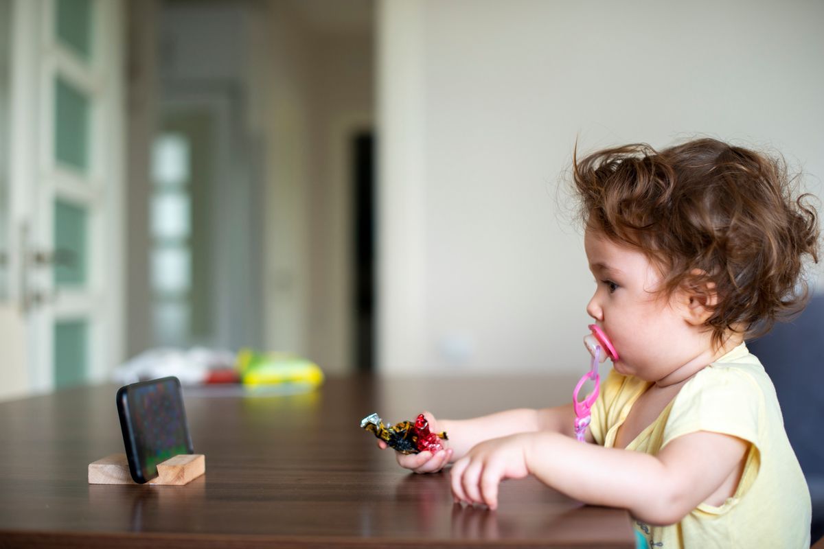 cute baby girl watching cartoons on smartphone lying on table. Cute baby girl holding colorful candies