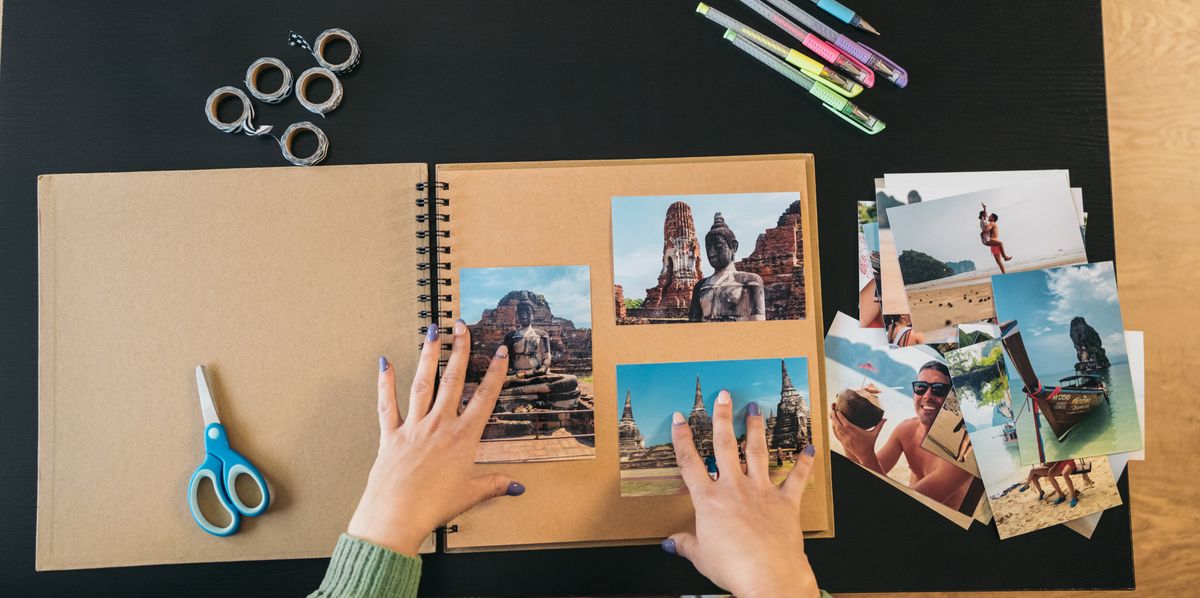 Image seen from above of a middle-aged woman's hands placing the photos and markers to make her handmade travel kraft paper photo album.
