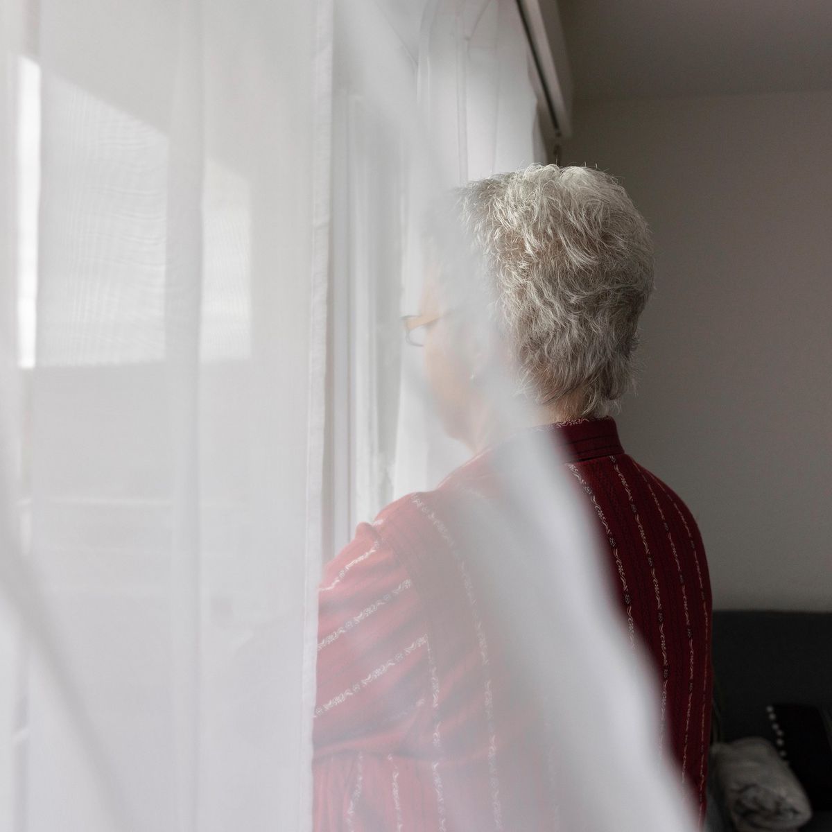 Frau steht nachdenklich am Fenster, Opfer eines Love-Scam-Betrugs, porträtiert von Susanne Keller.