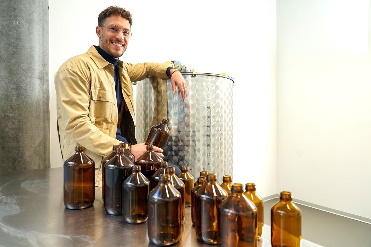 Karim Bakhti, fondateur de Colibrille, pose à côté de la cuve de 500 litres où sera brassé son produit de nettoyage, qui sera vendu dans des bouteilles en verre.