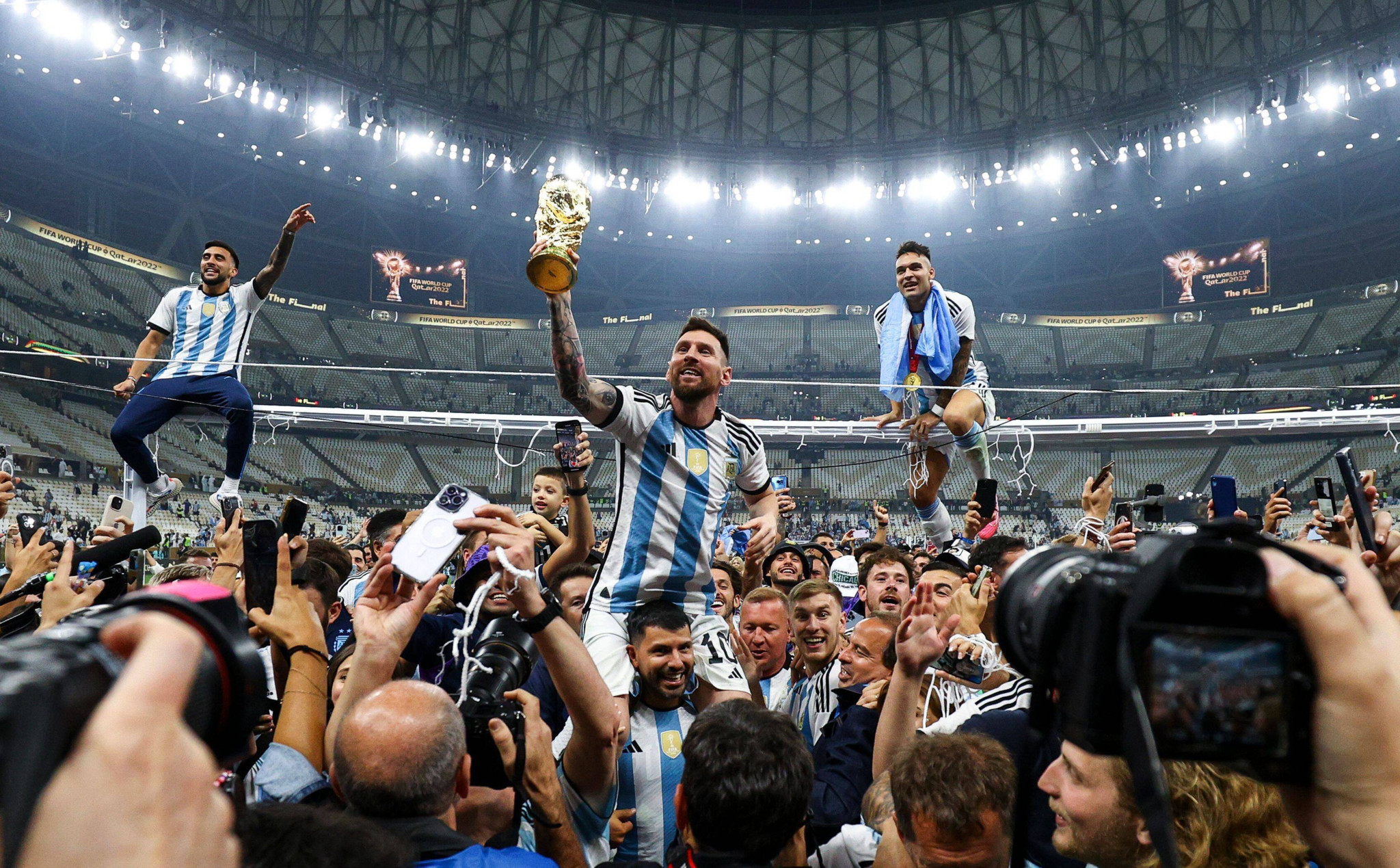 Lionel Messi hebt den Pokal, umgeben von jubelnden Teamkollegen und Fans, nach dem Gewinn der Fussball-Weltmeisterschaft 2022 im Lusail-Stadion in Katar.