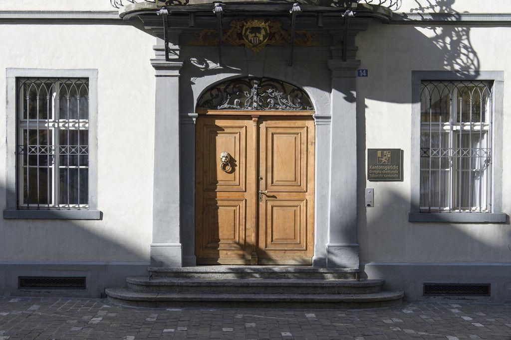 Entrée en bois élégante avec des détails sculptés, encadrée par des fenêtres à barreaux en fer forgé sur une façade claire.