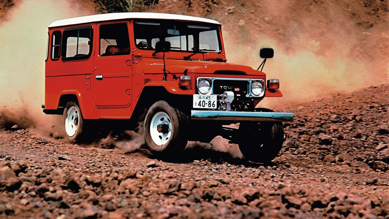 Klassischer roter Toyota Land Cruiser FJ40 fährt über steiniges Gelände und wirbelt Staub auf – Ikone seit 75 Jahren.