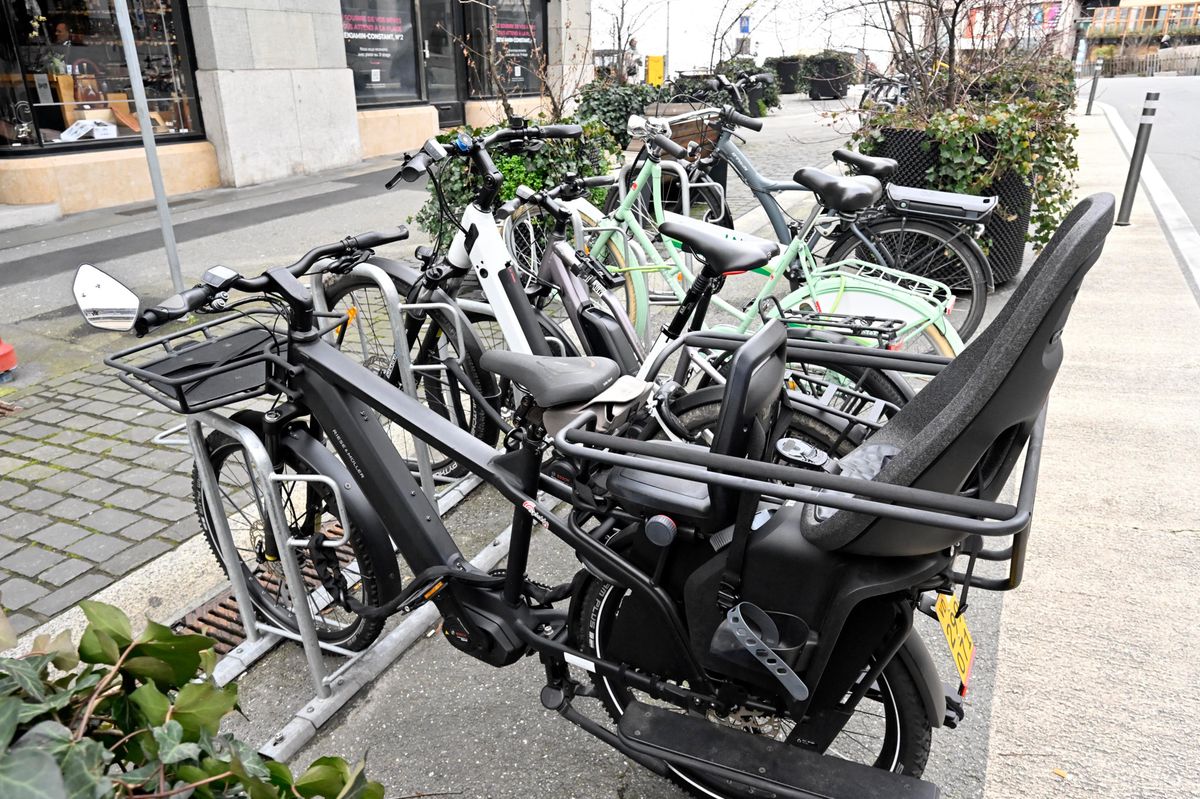 Plusieurs vélos électriques stationnés sur un trottoir à Lausanne, avec des bâtiments et des magasins en arrière-plan, le 27 février 2024.