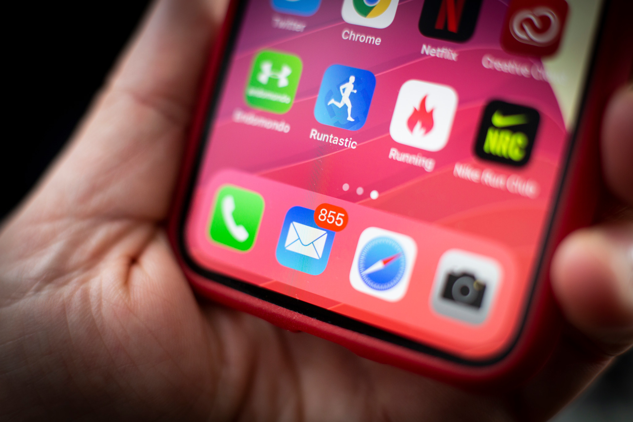 Hand hält rotes iPhone mit Mail-App-Symbol und 855 ungelesenen Nachrichten auf dem Startbildschirm.