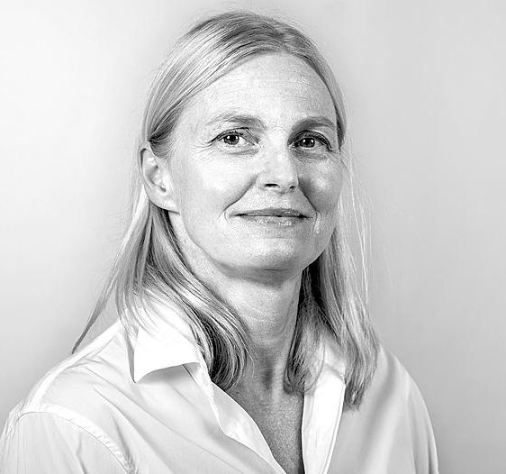 Portrait en noir et blanc de Priska Amstutz, portant une chemise blanche, regardant l'objectif avec un léger sourire.