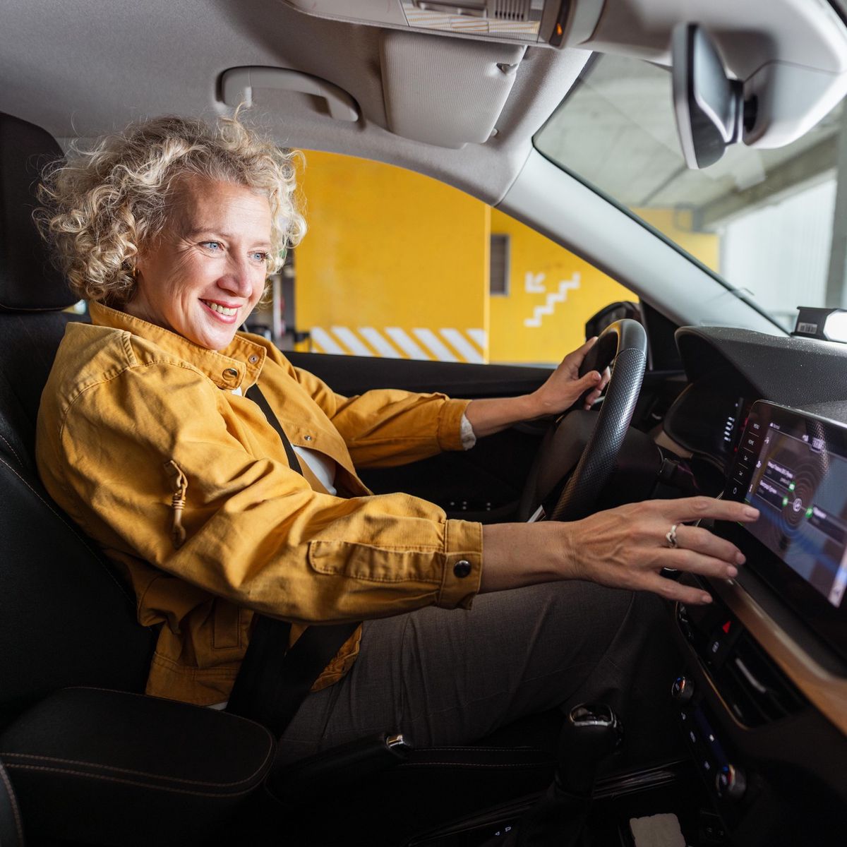 Une femme souriante dans sa voiture cherche une bonne station de radio en allant au travail.