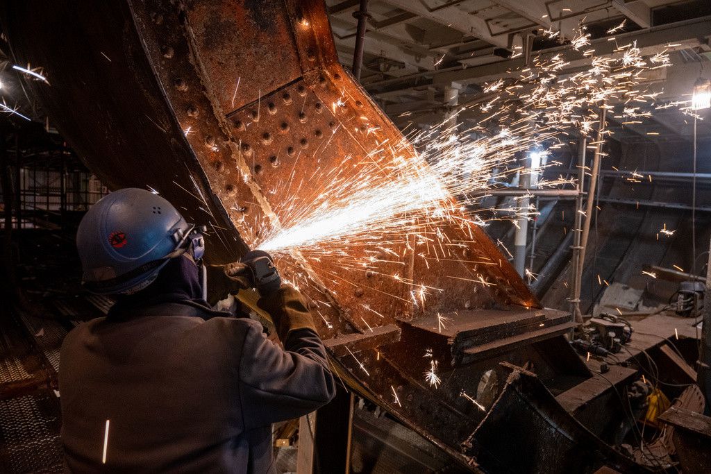 PRODUKTION - 01.12.2023, Mecklenburg-Vorpommern, Stralsund: Arbeiter setzen eine Platte in der Mitte des Segelschiff "Gorch Fock 1" wieder ein, die zur Entfernung von Maschinenteilen herausgenommen war. Derzeit steht der Segler zu großen Teilen eingerüstet in der großen Schiffbauerhalle des Maritimen Industrie- und Gewerbeparks Volkswerft. Insgesamt mussten nach Angaben der Stadt, der die 90 Jahre alte Dreimastbark seit diesem Jahr gehört, etwa 70 Quadratmeter Außenhaut getauscht werden. Seit Juni befindet sich das Schiff auf der Stralsunder Volkswerft. Für rund 10 Millionen Euro soll die Schwimmfähigkeit für die kommenden 25 Jahre, die Sicherheit der Takelage und der Brandschutz sichergestellt werden. Foto: Stefan Sauer/dpa +++ dpa-Bildfunk +++ (KEYSTONE/DPA/Stefan Sauer)