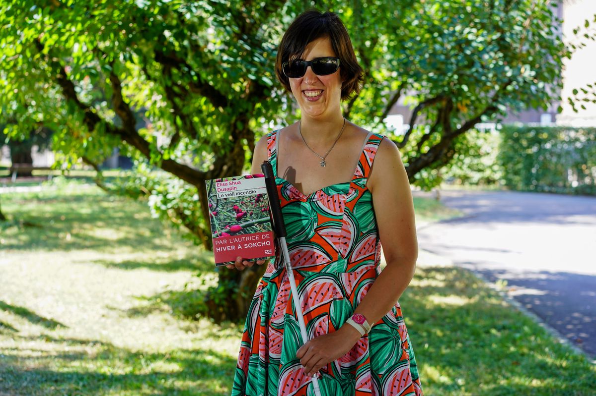 Malvoyante de naissance, Céline Witschard pose avec le dernier livre d’Elisa Shua Dusapin, «Le vieil incendie», paru mardi chez Zoé. Le même livre existe sur la médiathèque numérique MonaLira. 