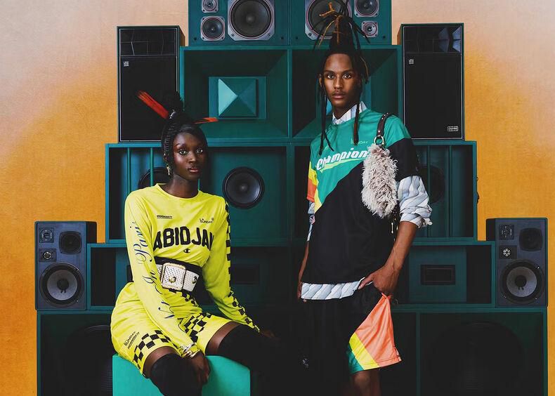 Deux personnes posent devant une installation de haut-parleurs multicolores, vêtues de tenues modernes et colorées.