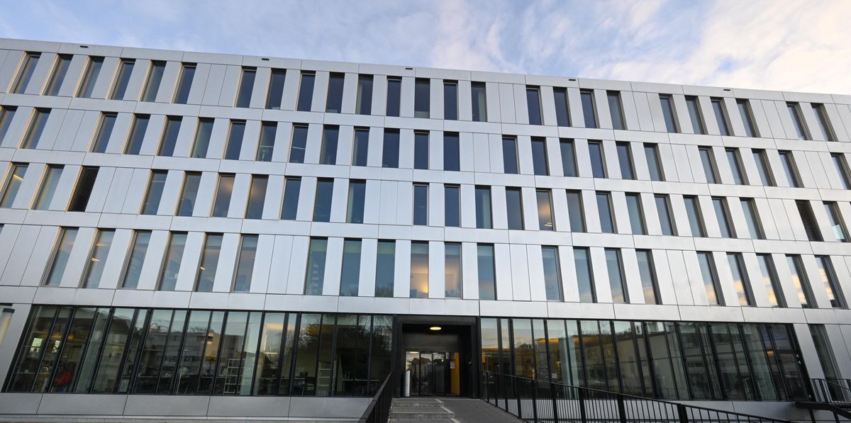 Façade moderne d'un bâtiment en métal et verre avec de multiples fenêtres et une entrée principale au centre accessible par une rampe.