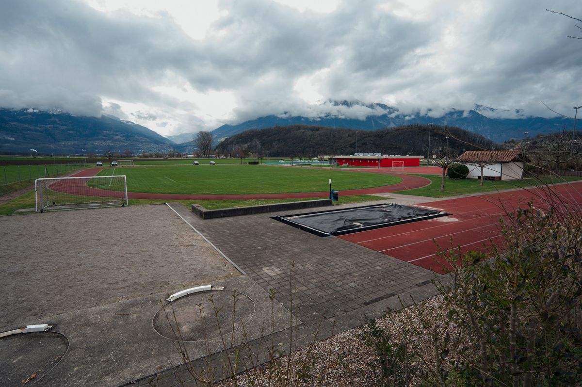 Piste d'athlétisme et terrain de sport à Ollon avec des montagnes en arrière-plan, sous un ciel nuageux.